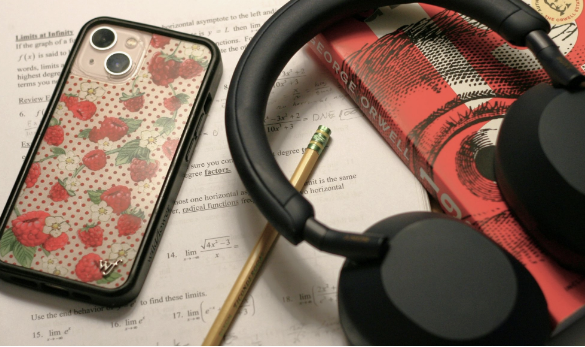 Photo of phone and headphones atop schoolwork and book. 
